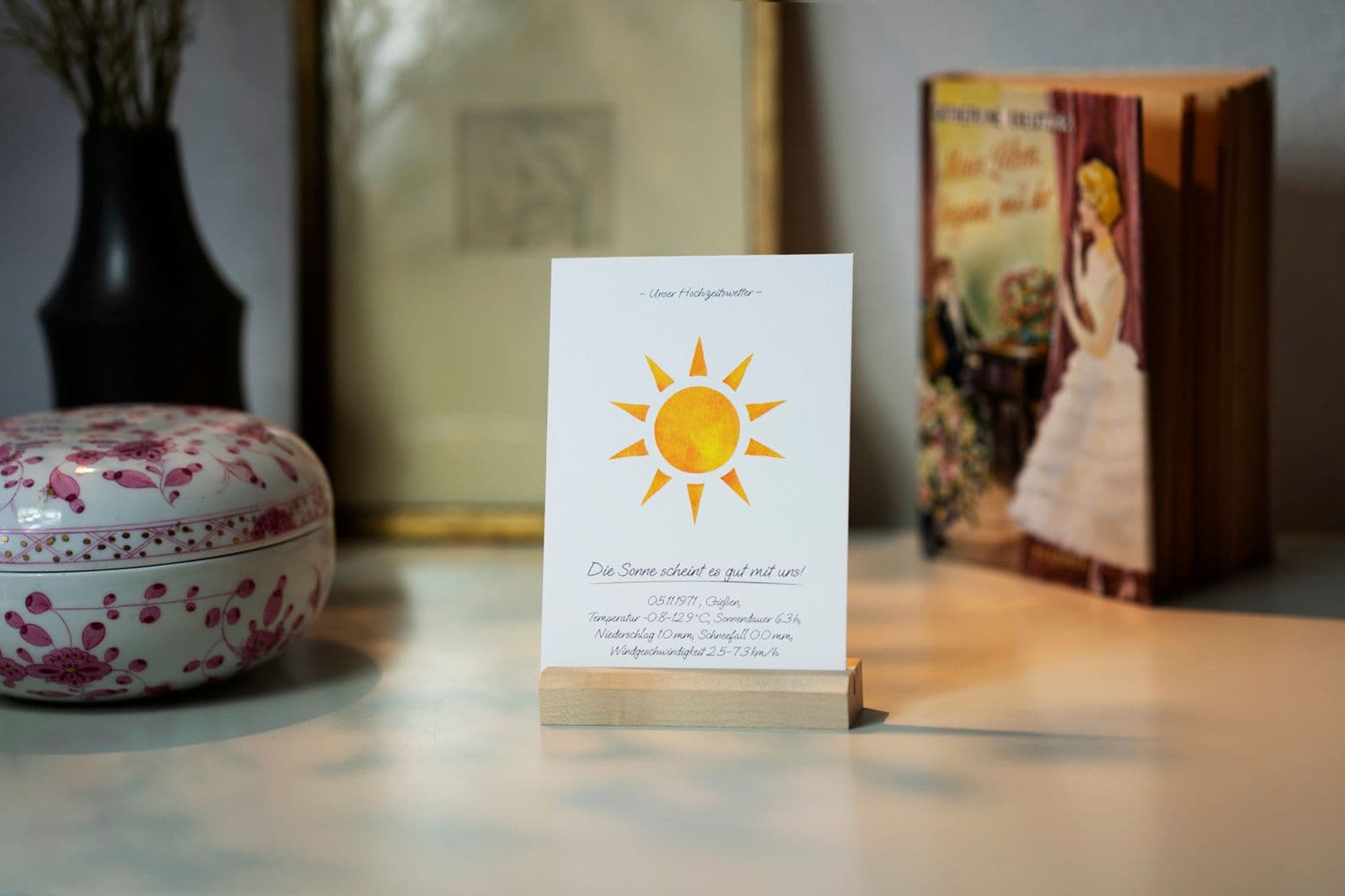 A postcard featuring a sun motif is displayed in a stand on a decorated sideboard