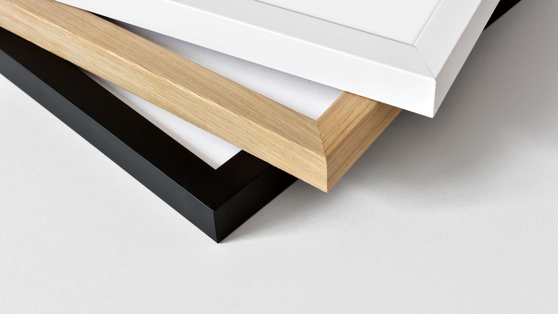 Detailed photo of the overlapping corners of a white, a wood-colored, and a black picture frame.